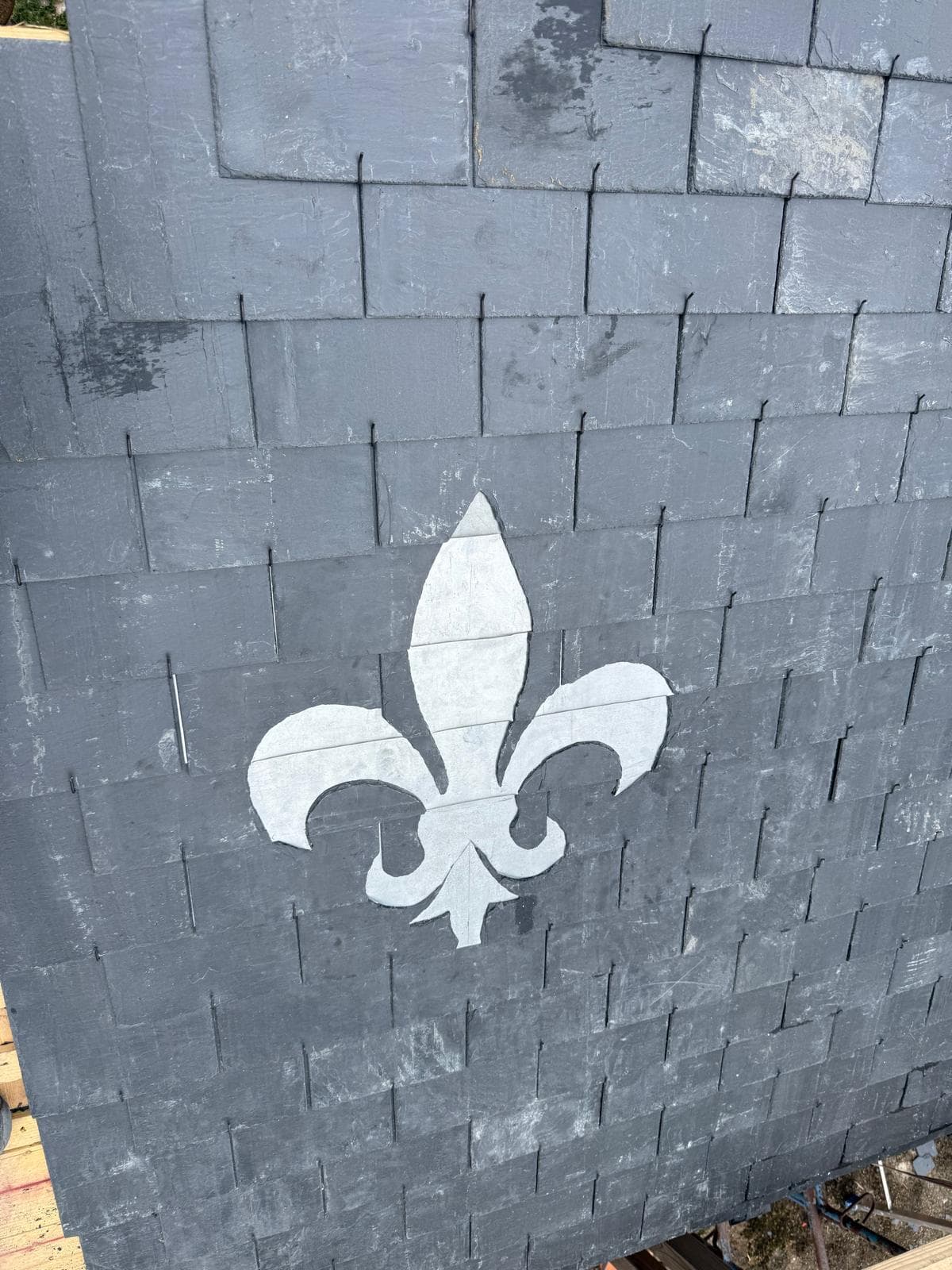 Fleur de lys en ardoise claire, incrustée dans le versant